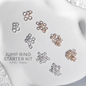 May include: A Jump Ring Starter Kit with 120 pieces. The image shows various jump rings in silver, gold, and rose gold tones. The jump rings are arranged on a white surface.