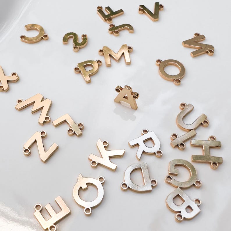 May include: Assortment of gold-colored metal letter charms with two holes for attaching to jewelry or other crafts. Letters include A, B, C, D, E, F, G, H, I, J, K, L, M, N, O, P, Q, R, S, T, U, V, W, X, Y, and Z.
