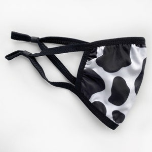 May include: Black and white cow print face mask with adjustable ear loops. The mask is made of a soft, breathable fabric.