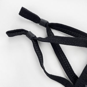 May include: Close-up of black adjustable straps with stitching detail. The straps are crossed and tied together.