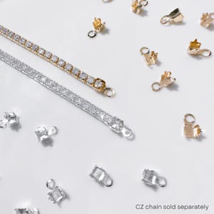 May include: A gold and silver CZ chain with matching clasps and connectors. The gold chain is adorned with clear, round gemstones. The silver chain also features clear, round gemstones. Various gold and silver clasps and connectors are scattered around the chains.