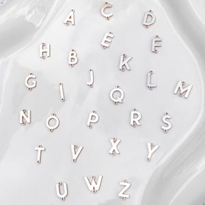May include: A set of 26 silver metal alphabet letter charms. Each letter is separate and has a hole for attaching to a chain or bracelet.