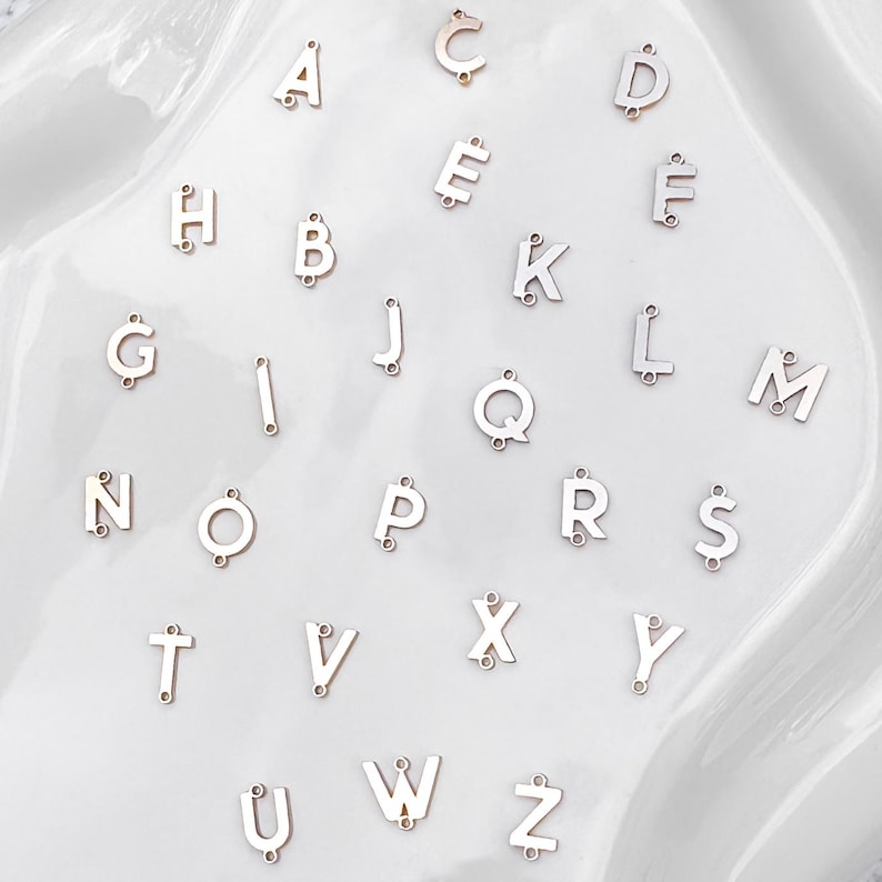 May include: A set of 26 silver metal alphabet letter charms. Each letter is separate and has a hole for attaching to a chain or bracelet.