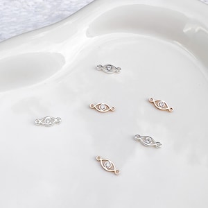 May include: Five silver and gold evil eye charms with clear crystal accents. The charms are in the shape of an eye and have a loop on each end for attaching to jewelry.