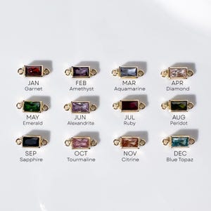 May include: Gold-toned rectangular birthstone charms with various colored gemstones, including garnet, amethyst, aquamarine, and diamond. Each charm is labeled with a month and gemstone name. The charms are displayed on a white background.