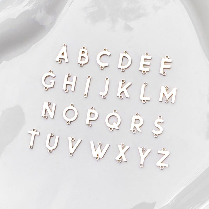 May include: A set of 26 white metal alphabet letter charms. Each letter is separate and has a hole for attaching to a necklace, bracelet, or other jewelry.