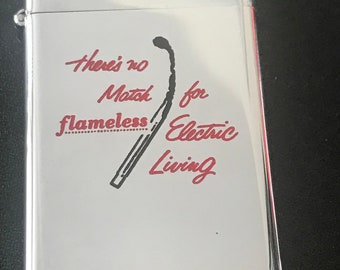 May include: A silver-colored lighter with the text "There's no Match for flameless Electric Living" in red script. A stylized match graphic is next to the text. The lighter has a shiny, reflective surface.