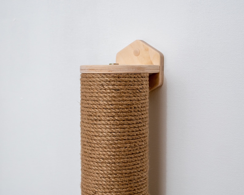 Puede incluir: Un rascador de sisal marr&oacute;n para gatos, montado en una pared con un soporte de madera. El poste est&aacute; envuelto en cuerda de sisal natural.