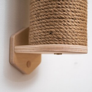 Puede incluir: Un rascador para gatos de madera con una cubierta de cuerda natural. El poste est&aacute; montado en una pared con una base hexagonal de madera.