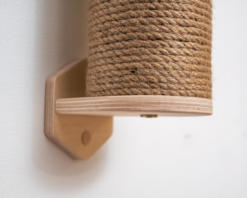Puede incluir: Un rascador para gatos de madera con una cubierta de cuerda natural. El poste est&aacute; montado en una pared con una base hexagonal de madera.