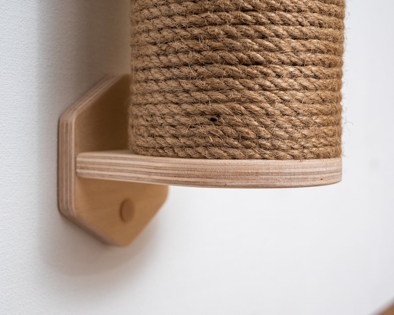 Puede incluir: Un rascador para gatos de madera con una cubierta de cuerda natural. El poste est&aacute; montado en una pared con un soporte de madera.