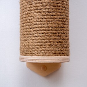 Puede incluir: Un rascador de cuerda de sisal marr&oacute;n para gatos, montado en una pared con una base de madera.