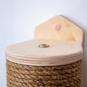 Puede incluir: Un rascador para gatos de madera con una base cubierta de cuerda y una plataforma de madera en la parte superior. La plataforma tiene un tornillo en el centro.