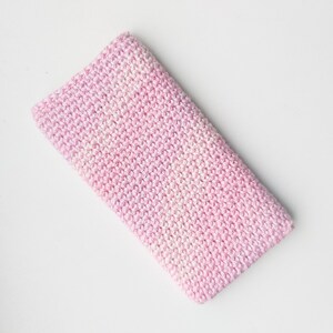 Puede incluir: Una manta de bebé de crochet rosa y blanco. La manta está hecha con un hilo suave y texturizado y tiene un sutil efecto degradado.