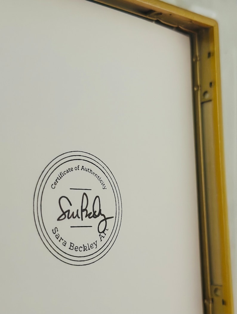 K&ouml;nnte beinhalten: Ein gerahmtes Kunstwerk mit einem goldfarbenen Metallrahmen. Das Kunstwerk hat einen wei&szlig;en Hintergrund mit einem kreisf&ouml;rmigen schwarzen Stempel mit der Aufschrift "Certificate of Authenticity" und der Signatur des K&uuml;nstlers "Sara Beckley Art."