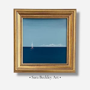 May include: A square painting in a gold frame featuring a small sailboat on a dark blue sea under a light blue sky. The horizon line separates the two shades of blue, and a faint white cloud formation is visible in the distance. Text reads Sara Beckley Art.