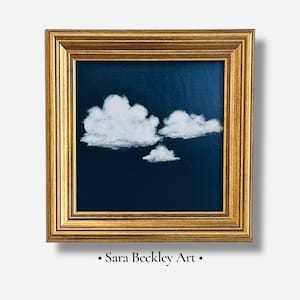 May include: A framed painting featuring three white fluffy clouds against a dark blue background. The artwork is enclosed in a gold-colored, ornate frame. The text "Sara Beckley Art" is at the bottom.