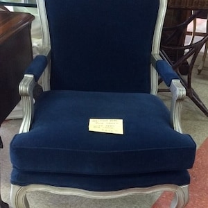May include: A navy blue upholstered armchair with silver-painted wooden frame. The chair has a curved back, armrests, and a cushioned seat. A yellow sticky note is attached to the seat. The chair is a piece of furniture.
