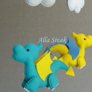 May include: A baby mobile with two felt dragons, one blue and one yellow, with white clouds hanging above. The dragons have yellow wings and blue accents.