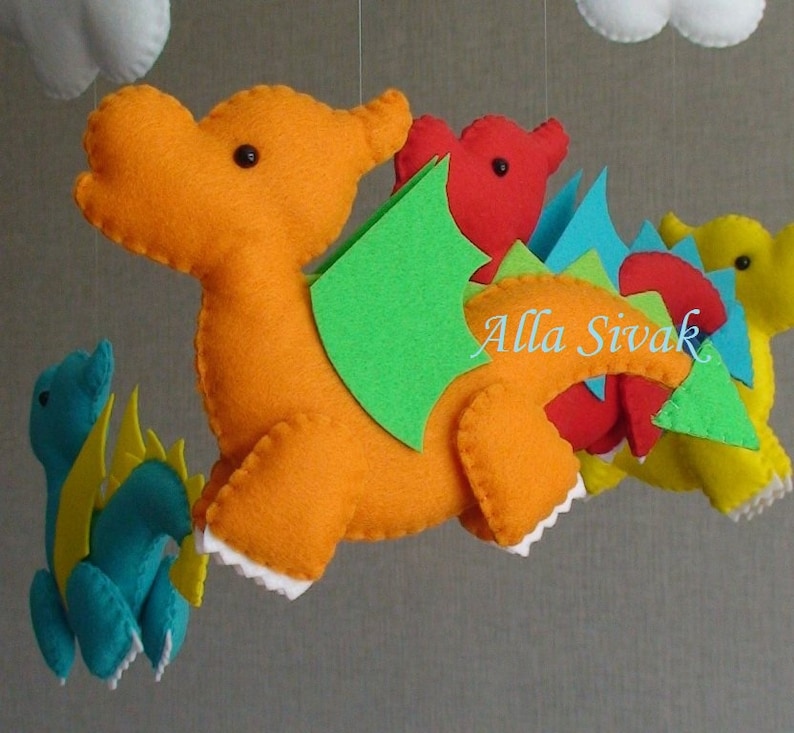 May include: A felt mobile with four colorful dragons. The largest dragon is orange with green wings and a red tail. The other dragons are red, blue, and yellow.