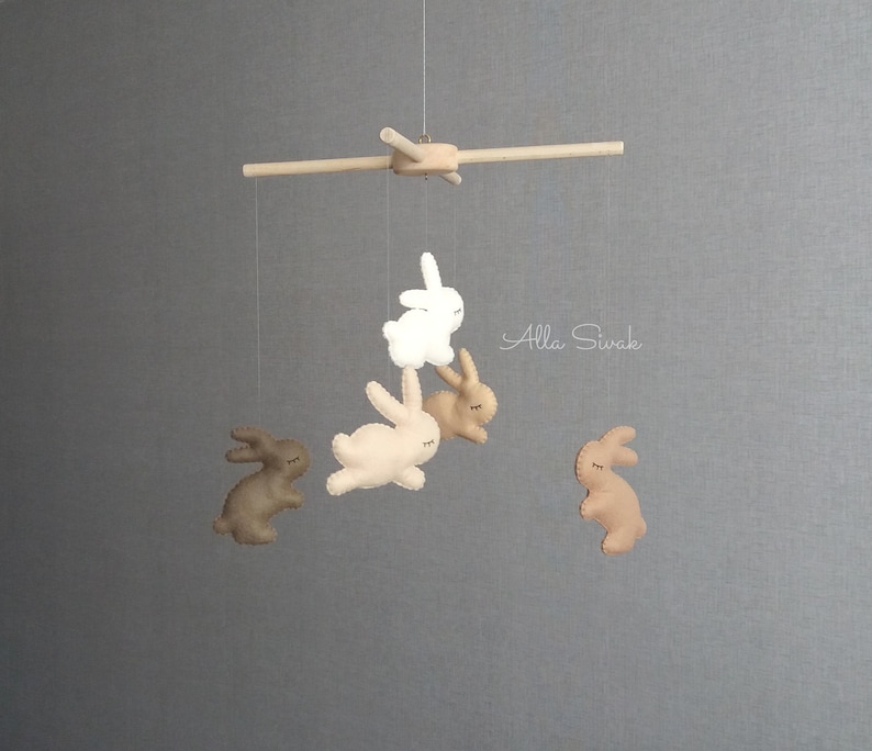 May include: A wooden mobile with five felt bunny toys hanging from it. The bunnies are in shades of brown and white. The mobile is hanging from a wooden rod.