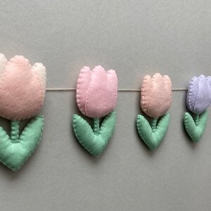 May include: A garland of felt tulips in pink, light purple, and green. The garland is strung on a white thread and would be a cute addition to a nursery or child's room.