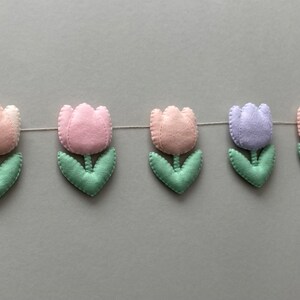 May include: A garland of felt tulips in pink, light purple, and green. The garland is strung together with white thread.