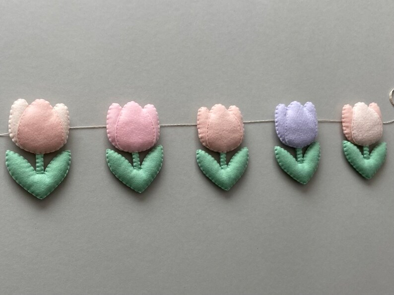 May include: A garland of felt tulips in pink, light purple, and green. The garland is strung together with white thread.