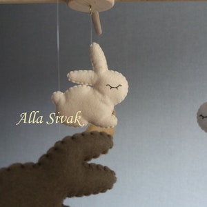 May include: A mobile with three felt bunny toys. Two bunnies are white with black eyes and the third bunny is brown with black eyes. The mobile is hanging from a wooden dowel.