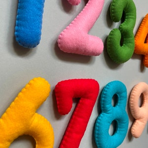 May include: Felt numbers from one to nine in different colours. The numbers are sewn together with a zig-zag stitch.