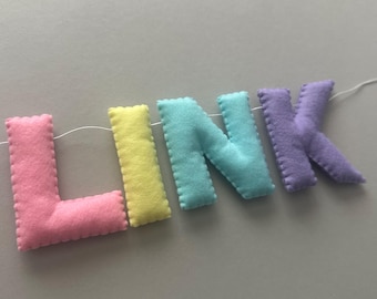 May include: A felt banner with the word "LINK" spelled out in pastel colours. The letters are pink, yellow, blue, and purple.