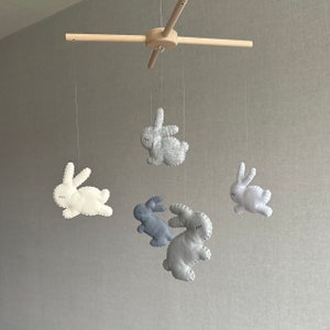 May include: A wooden mobile with five felt bunny toys. The bunnies are in shades of gray and white. The mobile is suspended from a wooden crossbar.