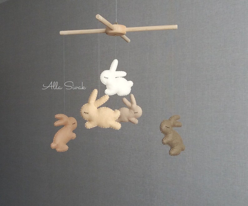 May include: A wooden mobile with five felt bunny toys. The bunnies are in shades of brown and white. The mobile is hanging from a wooden crossbar.