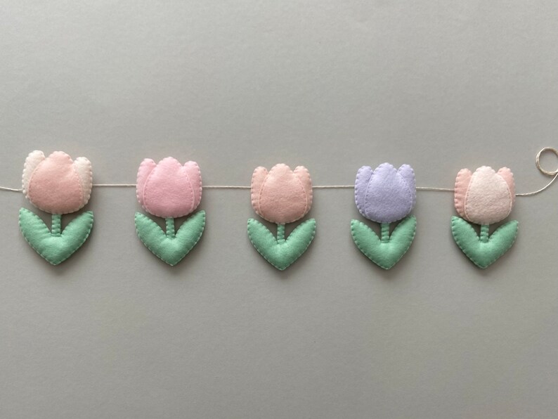May include: A garland of felt tulips in pink, light pink, lavender, and green. The tulips are strung together with white thread.