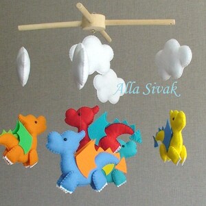 May include: A baby mobile with five hanging felt toys: four colorful dragons and three white clouds. The dragons are red, orange, blue, and yellow. The mobile is suspended from a wooden frame.