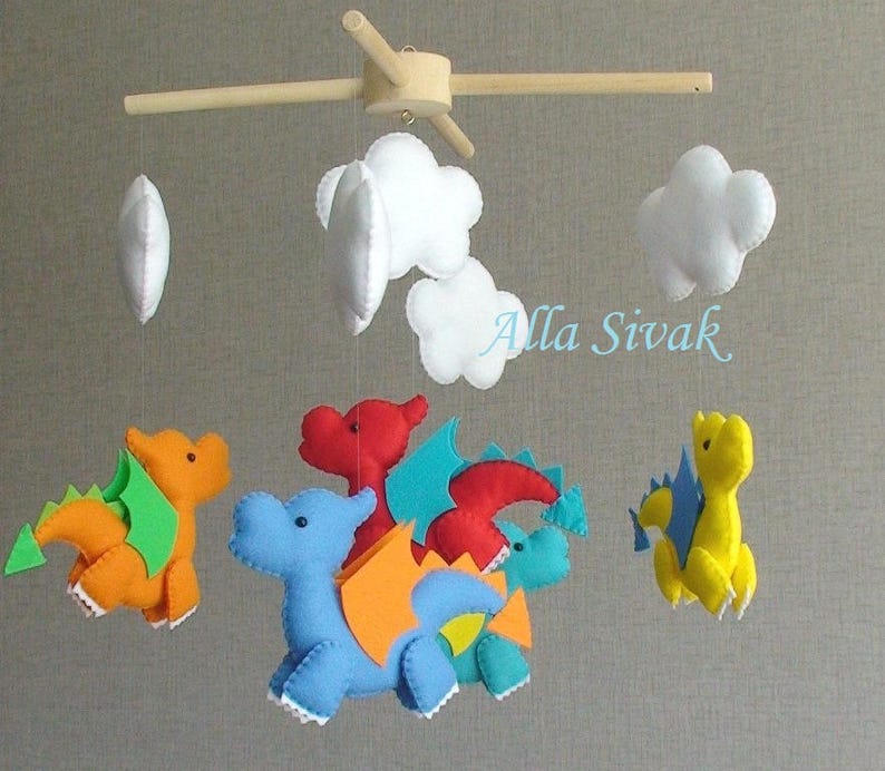 May include: A baby mobile with five hanging felt toys: four colorful dragons and three white clouds. The dragons are red, orange, blue, and yellow. The mobile is suspended from a wooden frame.