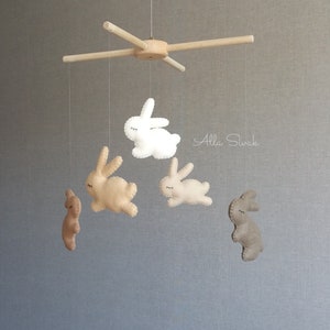 May include: A wooden mobile with five felt bunny toys hanging from it. The bunnies are in shades of brown and white. The mobile is suspended from a wooden frame. The text "Alla Sivak" is visible in the background.