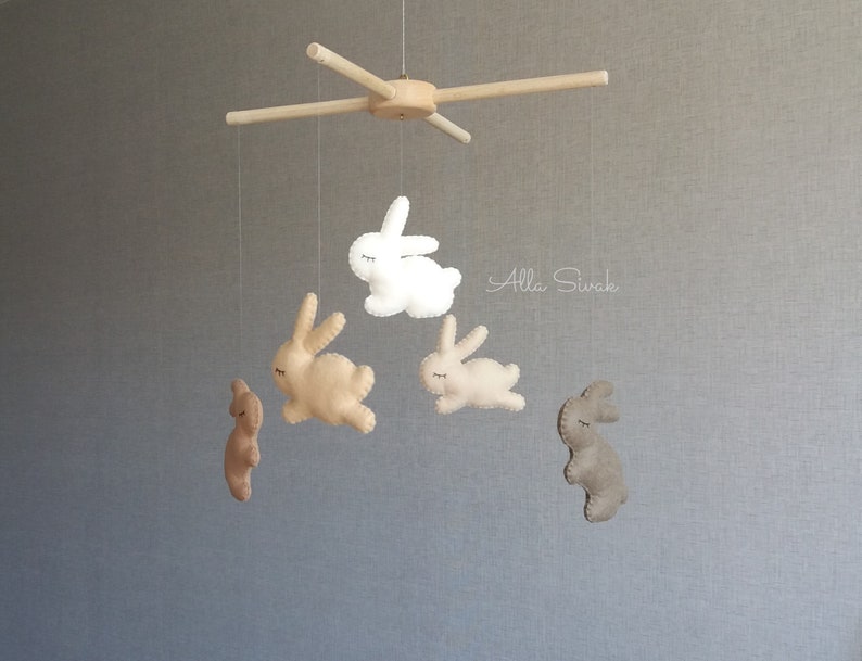 May include: A wooden mobile with five felt bunny toys hanging from it. The bunnies are in shades of brown and white. The mobile is suspended from a wooden frame. The text "Alla Sivak" is visible in the background.