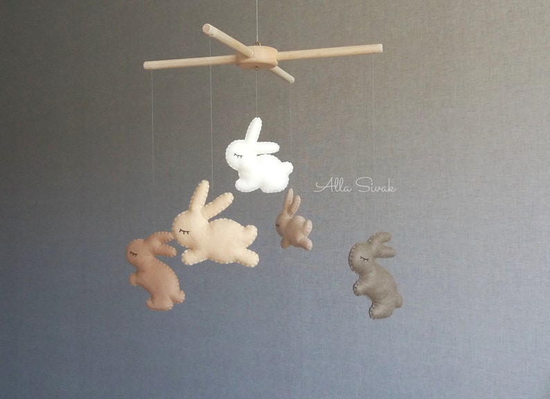 May include: A wooden mobile with five felt bunny toys hanging from it. The bunnies are in shades of brown and white. The mobile is suspended from a wooden crossbar.