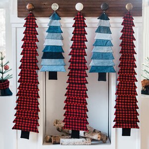 May include: Five fabric Christmas trees hanging on a wall. Two trees are red and black plaid, and three trees are blue denim. The trees are all the same size and shape.