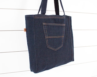 May include: A dark blue denim tote bag with a large front pocket. The bag has brown leather accents and a top handle.