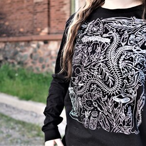 Pode incluir: Camiseta preta de manga comprida com uma estampa gr&aacute;fica branca de um esqueleto, plantas e outras imagens m&iacute;sticas.