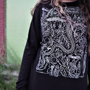 Pode incluir: Camiseta preta de manga comprida com uma estampa gr&aacute;fica branca de um esqueleto, plantas e outras imagens m&iacute;sticas. A estampa inclui o texto "The Moon".