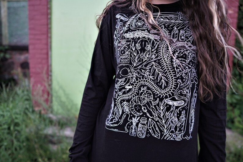 Pode incluir: Camiseta preta de manga comprida com uma estampa gr&aacute;fica branca de um esqueleto, plantas e outras imagens m&iacute;sticas. A estampa inclui o texto "The Moon".