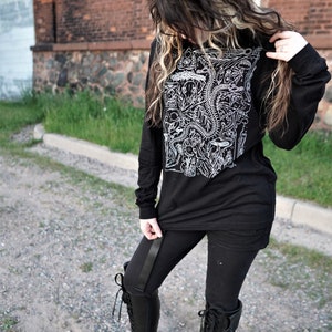 Pode incluir: Uma camisa preta de manga comprida com uma estampa gr&aacute;fica branca de v&aacute;rias ilustra&ccedil;&otilde;es anat&ocirc;micas. A camisa &eacute; usada com leggings pretos e botas pretas de cano alto.