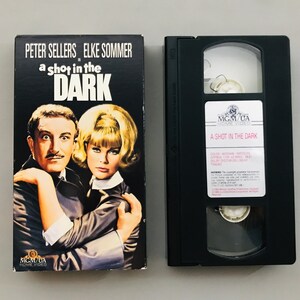 May include: A VHS tape case with a black background and a picture of Peter Sellers and Elke Sommer on the front. The title of the movie is "A Shot in the Dark" and the case is labeled "MGM/UA Home Video".