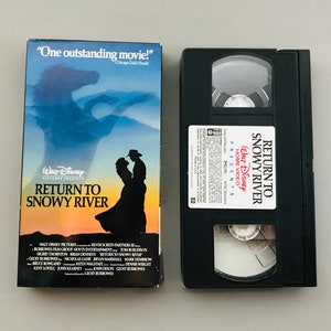 May include: A VHS tape of the movie "Return to Snowy River" featuring a silhouette of a couple against a sunset backdrop. The text "One outstanding movie!" is printed on the front cover.