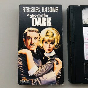 May include: A VHS tape case for the movie "A Shot in the Dark" starring Peter Sellers and Elke Sommer. The case features a photo of the actors on the front.