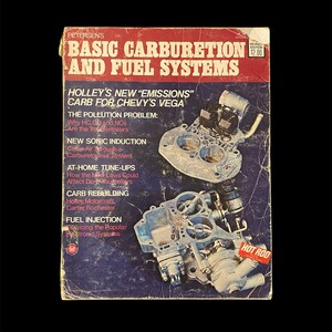 May include: A vintage book cover with a red and white title "Basic Carburetion and Fuel Systems". The cover features a diagram of a carburetor with the text "Holley's New "Emissions" Carb for Chevy's Vega" and "Hot Rod" in a red circle.