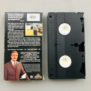 May include: A VHS tape case with a black background and a white label. The label features a photo of Peter Sellers, the title "A Shot in the Dark", and the text "Inspector Clouseau is in the fine and subtle form in which he first came and conquered us."